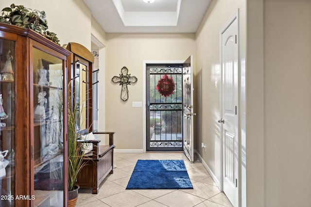 entryway featuring a tray ceiling, baseboards, and light tile patterned floors