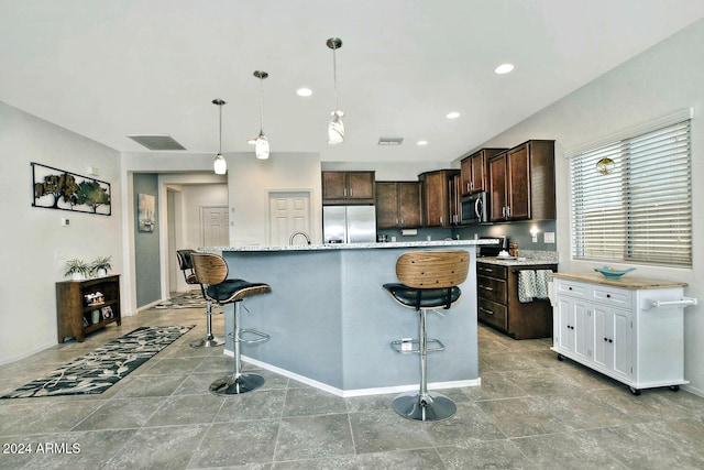 kitchen featuring an island with sink, appliances with stainless steel finishes, a breakfast bar area, dark brown cabinetry, and decorative light fixtures