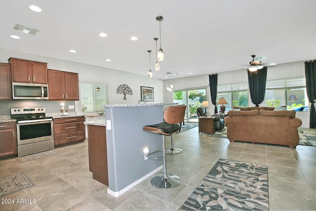 kitchen with an island with sink, stainless steel appliances, a kitchen bar, decorative light fixtures, and light stone counters