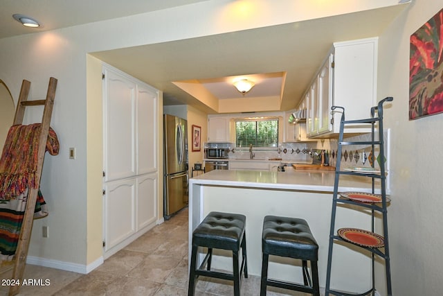 kitchen featuring stainless steel appliances, a breakfast bar, kitchen peninsula, and white cabinets