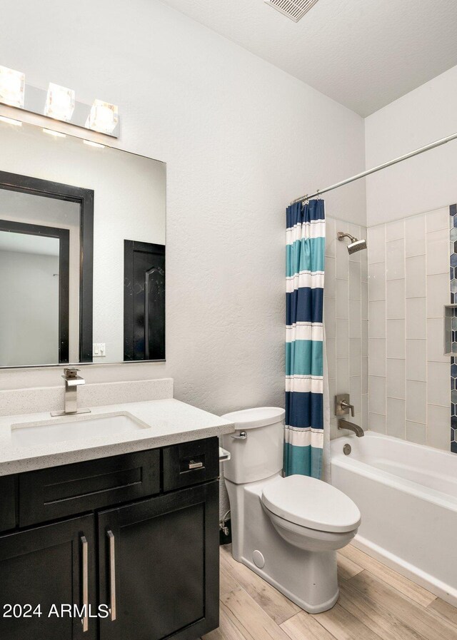 full bathroom featuring a textured ceiling, shower / bathtub combination with curtain, hardwood / wood-style floors, vanity, and toilet