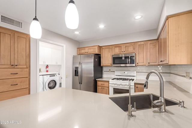 kitchen with sink, washer / dryer, stainless steel appliances, decorative backsplash, and decorative light fixtures