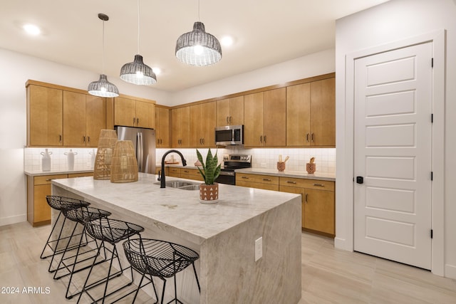 kitchen featuring sink, appliances with stainless steel finishes, pendant lighting, a kitchen island with sink, and decorative backsplash