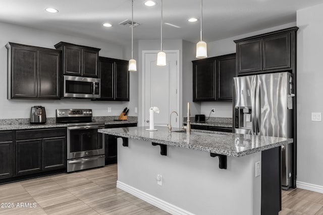 kitchen featuring appliances with stainless steel finishes, a center island with sink, a kitchen breakfast bar, and pendant lighting