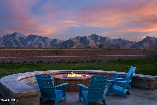 patio terrace at dusk with a fire pit, a mountain view, and a yard