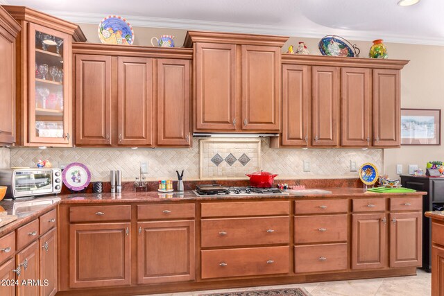 kitchen featuring dark stone countertops, light tile patterned floors, ornamental molding, stainless steel gas stovetop, and decorative backsplash