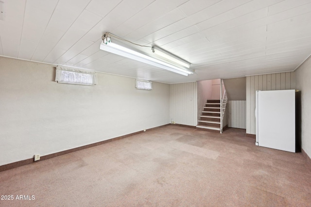 below grade area featuring carpet flooring, freestanding refrigerator, and stairway