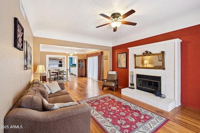 living room featuring ceiling fan with notable chandelier, wood finished floors, and a fireplace