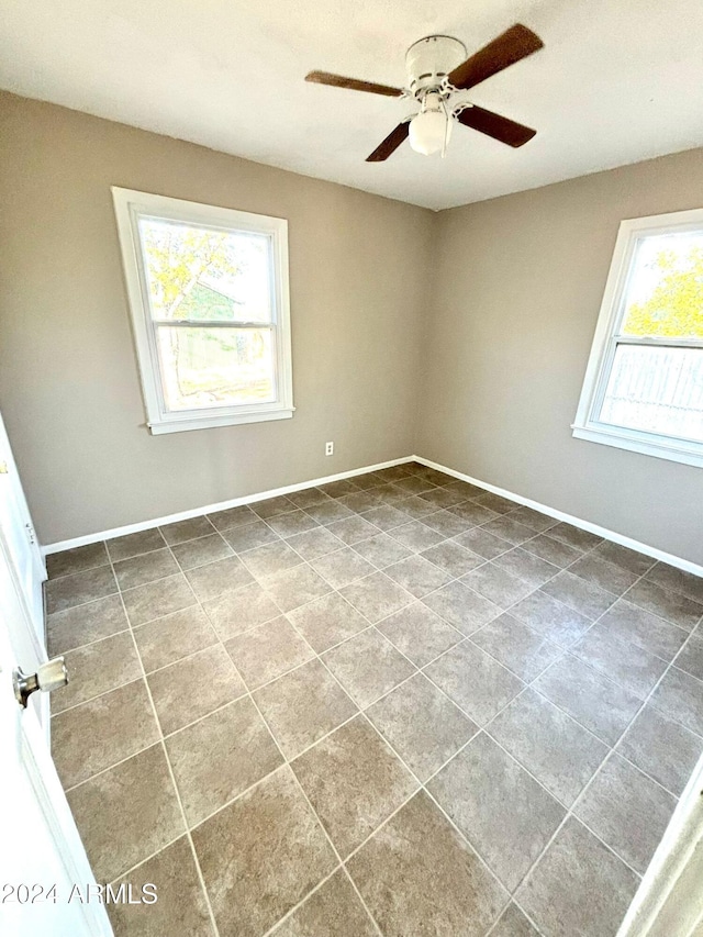 unfurnished room featuring ceiling fan, plenty of natural light, and dark tile patterned flooring