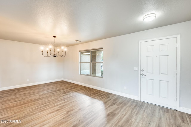 foyer entrance featuring light wood finished floors, visible vents, a textured ceiling, and baseboards