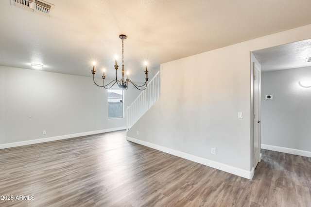 unfurnished dining area with visible vents, a textured ceiling, wood finished floors, baseboards, and a chandelier