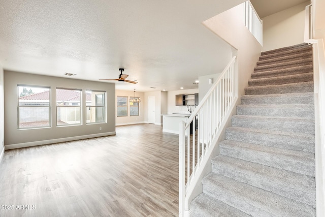 stairway with visible vents, baseboards, ceiling fan, wood finished floors, and a textured ceiling