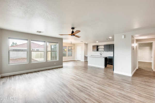 unfurnished living room featuring visible vents, baseboards, light wood-style floors, and ceiling fan with notable chandelier