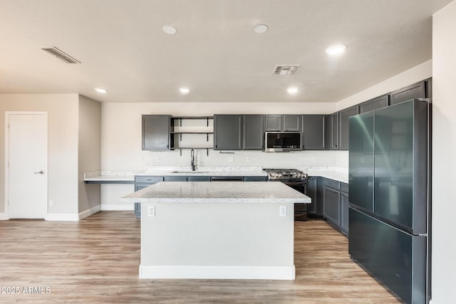 kitchen with visible vents, a kitchen island, appliances with stainless steel finishes, light wood-style floors, and a sink