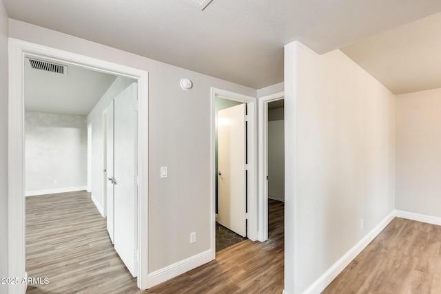 hallway featuring visible vents, baseboards, and wood finished floors