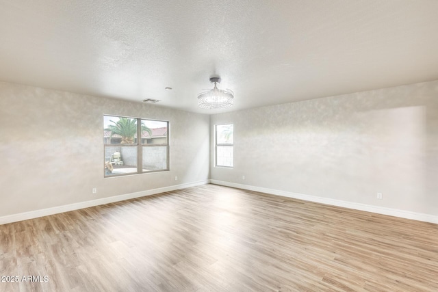 spare room with light wood finished floors, visible vents, a textured ceiling, and baseboards