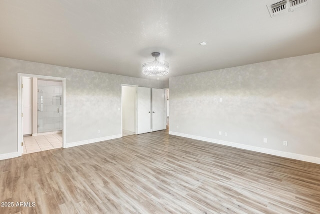 empty room with an inviting chandelier, baseboards, visible vents, and light wood-type flooring