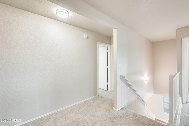 hall with an upstairs landing, baseboards, and carpet floors