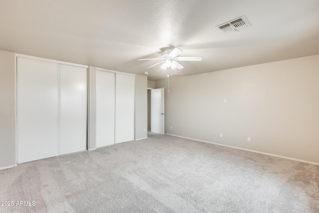 unfurnished bedroom with visible vents, two closets, a ceiling fan, a textured ceiling, and light colored carpet