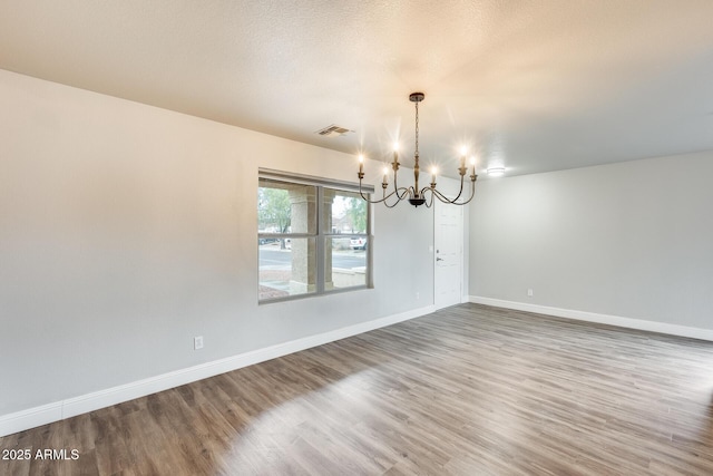 unfurnished room featuring visible vents, a textured ceiling, wood finished floors, baseboards, and a chandelier