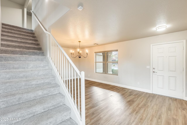 entrance foyer featuring baseboards, stairway, an inviting chandelier, wood finished floors, and a textured ceiling