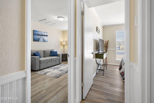 hallway featuring a wainscoted wall, ornamental molding, and wood finished floors