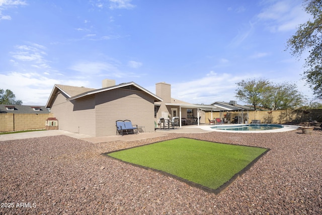 back of house featuring a patio, a fenced backyard, a fenced in pool, brick siding, and a chimney