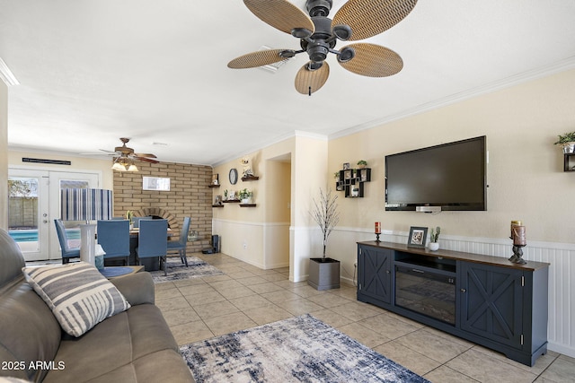 living room with light tile patterned floors, a wainscoted wall, ceiling fan, and crown molding