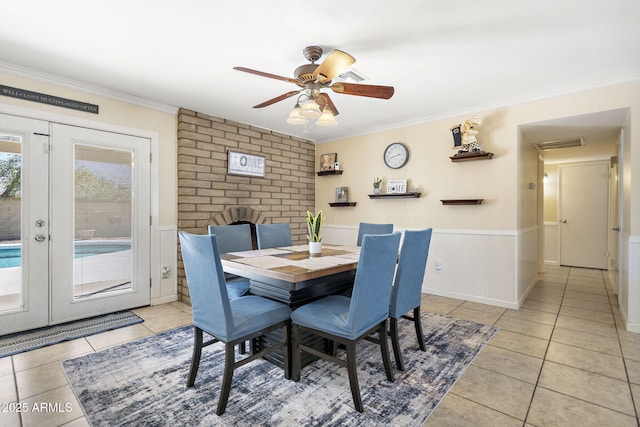 dining area with light tile patterned flooring, a wainscoted wall, and ornamental molding