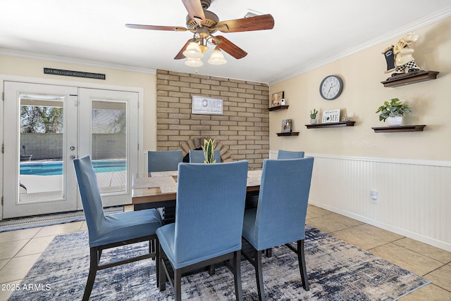 dining space with tile patterned flooring, crown molding, ceiling fan, and wainscoting