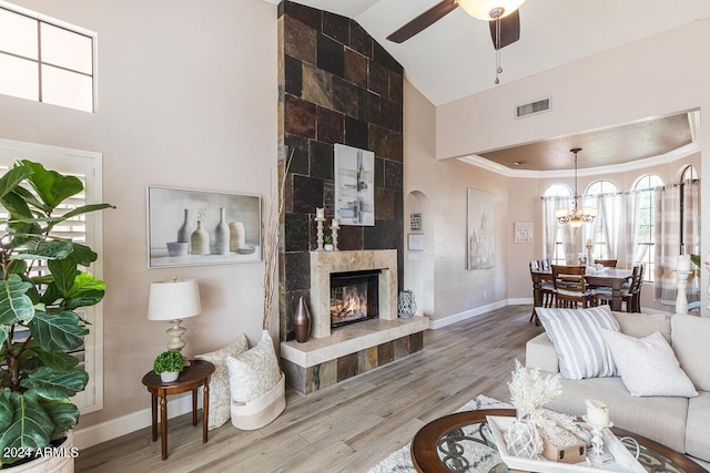 living room with ceiling fan with notable chandelier, vaulted ceiling, crown molding, hardwood / wood-style floors, and a tiled fireplace