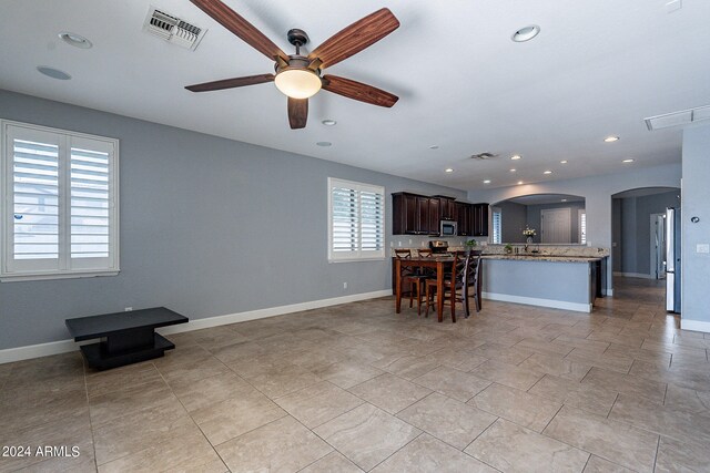 kitchen with ceiling fan, dark brown cabinets, light stone countertops, appliances with stainless steel finishes, and a kitchen bar