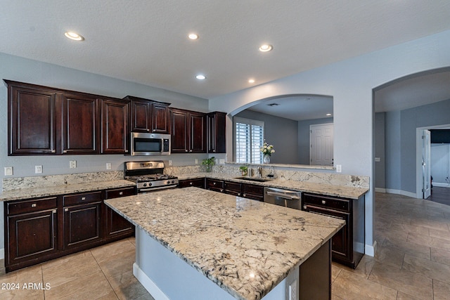 kitchen featuring sink, kitchen peninsula, a kitchen island, appliances with stainless steel finishes, and light stone countertops