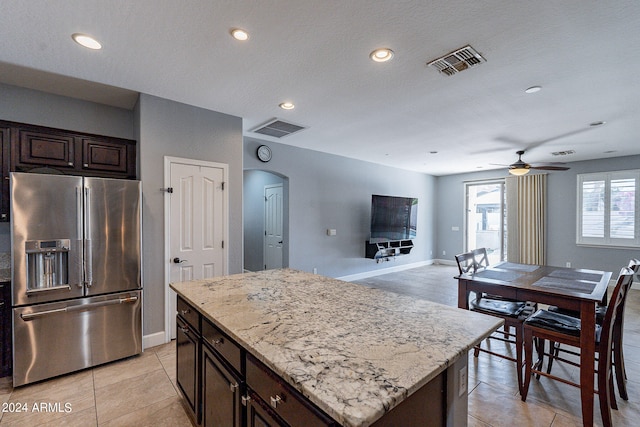 kitchen with light tile patterned flooring, stainless steel fridge, ceiling fan, dark brown cabinets, and a center island