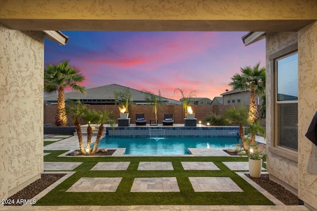 pool at dusk featuring pool water feature, a patio, and a lawn