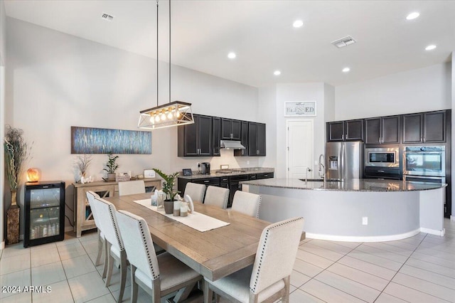 kitchen featuring stainless steel appliances, dark stone countertops, pendant lighting, a kitchen island with sink, and light tile patterned flooring