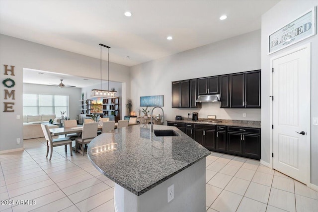 kitchen featuring a kitchen island with sink, sink, hanging light fixtures, ceiling fan, and dark stone countertops