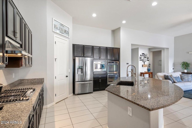 kitchen featuring dark stone counters, stainless steel appliances, sink, an island with sink, and light tile patterned flooring