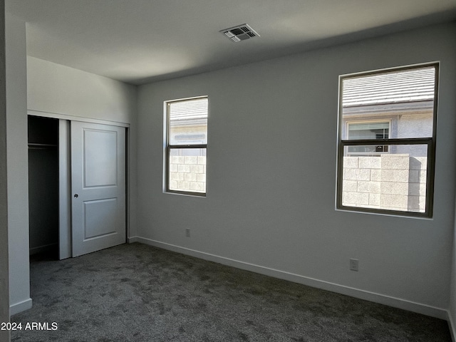 unfurnished bedroom with dark carpet and a closet