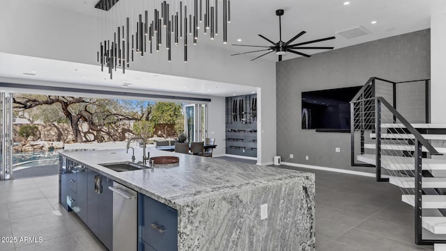 kitchen with ceiling fan, blue cabinetry, a sink, light stone counters, and open floor plan
