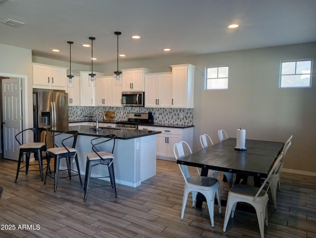 kitchen with appliances with stainless steel finishes, pendant lighting, an island with sink, and white cabinets