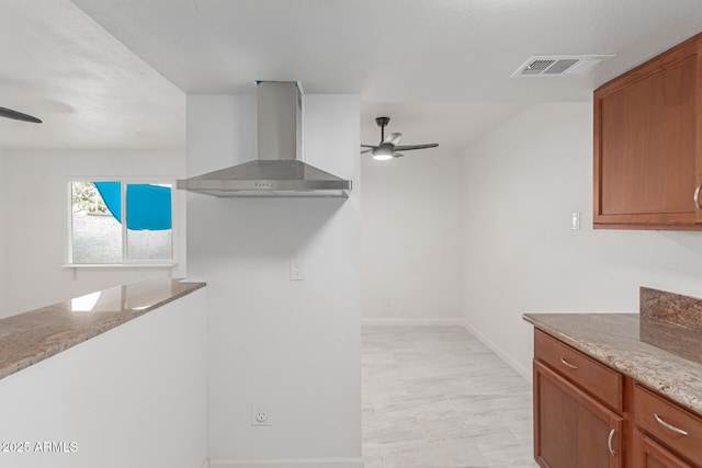 kitchen featuring light stone counters, ceiling fan, and wall chimney exhaust hood