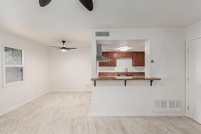 kitchen with a breakfast bar, sink, ceiling fan, kitchen peninsula, and wall chimney exhaust hood