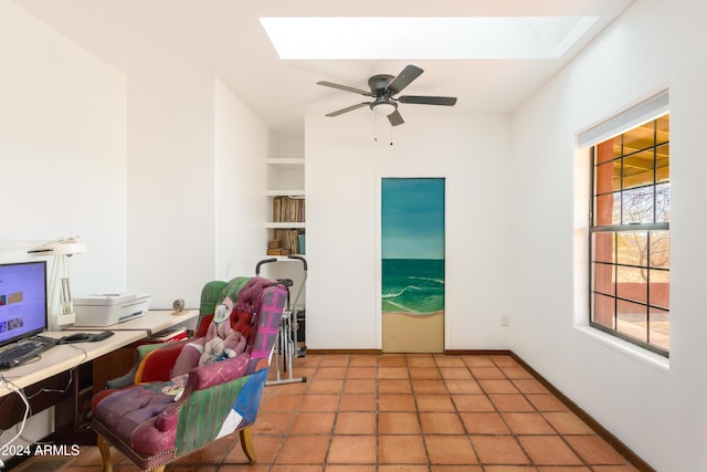 tiled office with built in shelves, ceiling fan, and a skylight