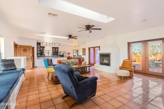 tiled living room with french doors, a skylight, track lighting, ceiling fan, and a tiled fireplace