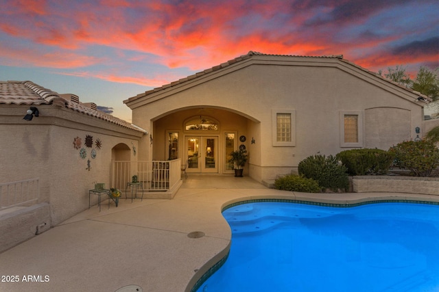 pool at dusk with a patio area and french doors