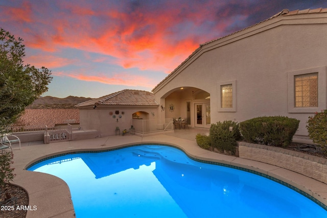 pool at dusk with a patio area and french doors