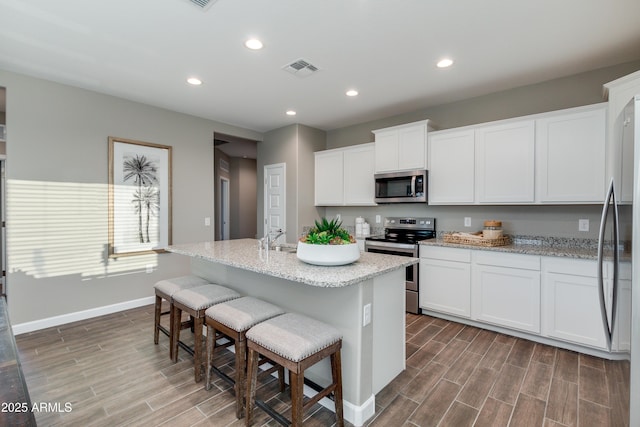 10619 W Bloch Rd, Tolleson, AZ 85353 - kitchen with appliances with stainless steel finishes, wood finished floors, white cabinets, recessed lighting, and a kitchen bar