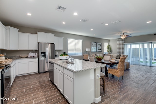 10619 W Bloch Rd, Tolleson, AZ 85353 - kitchen featuring stainless steel appliances, a center island with sink, white cabinets, open floor plan, and light stone counters
