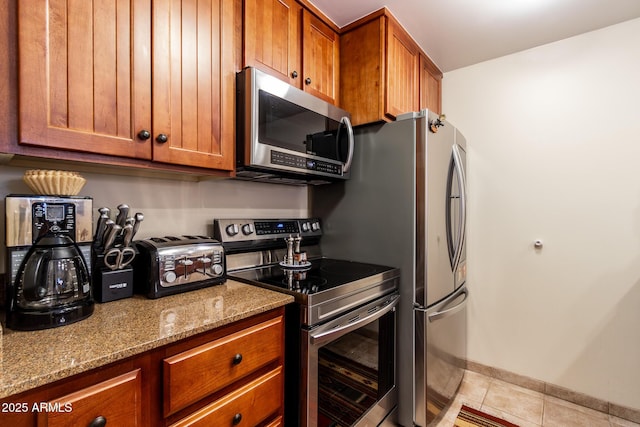 kitchen with stainless steel appliances, light tile patterned flooring, and light stone countertops